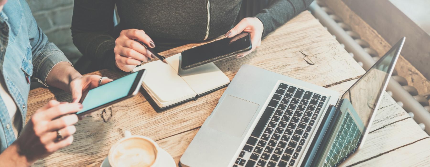 over head shot of women working on their phones with a laptop and planner in front of them